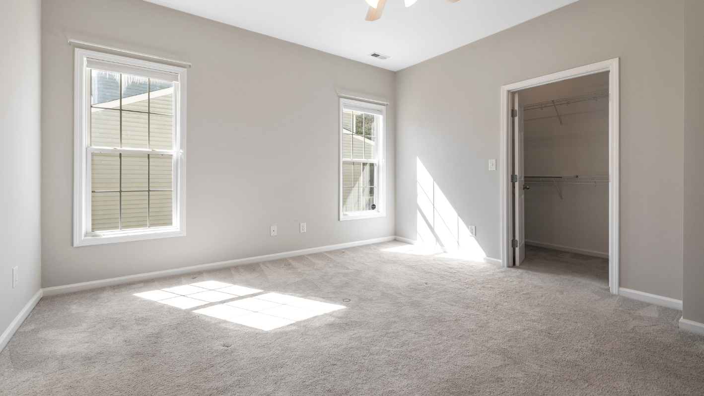 An empty room with a ceiling fan and two windows